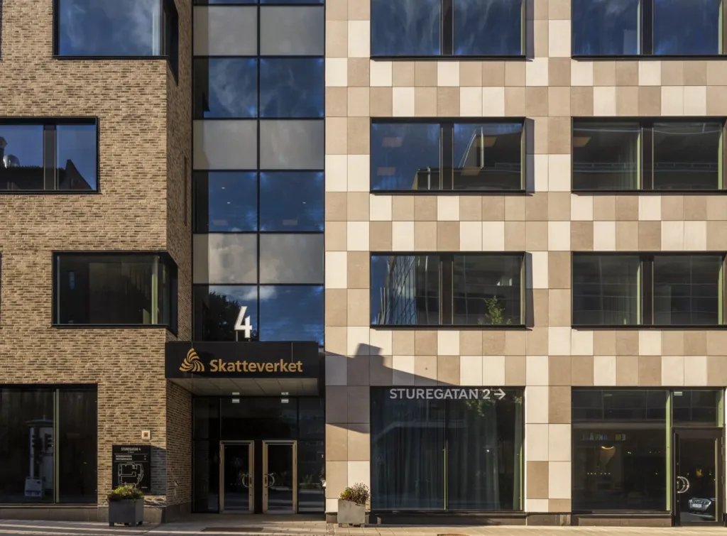 Entré till en byggnad med fasad av ljusa och mörka paneler, med skyltar som visar "Skatteverket" och "Studiefrämjandet".