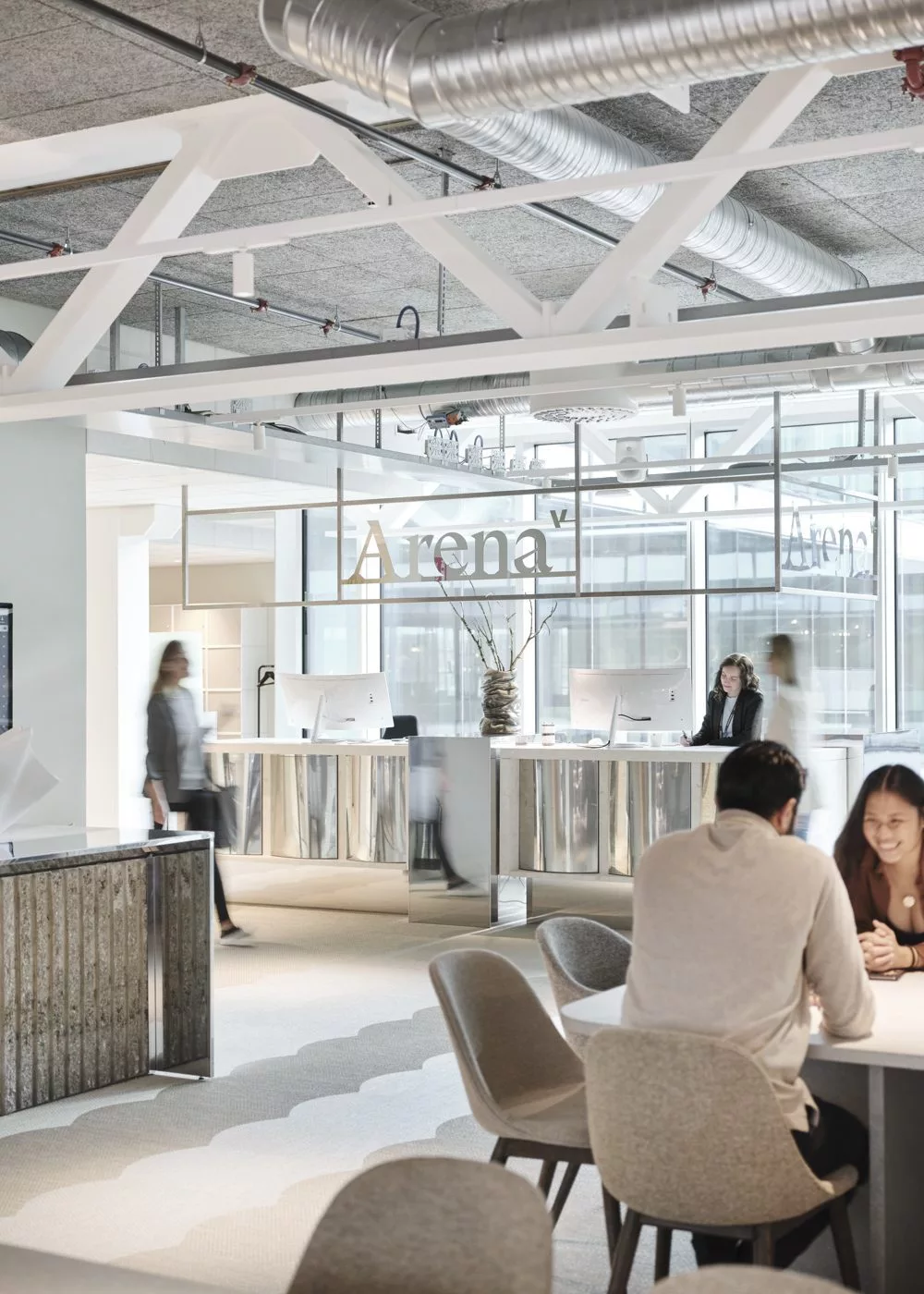 En modern reception med skylten "Arena" och flera personer som arbetar och samtalar.
