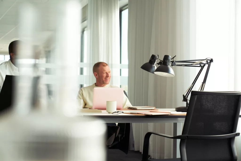 Man vid skrivbord ler och tittar ut genom fönstret
