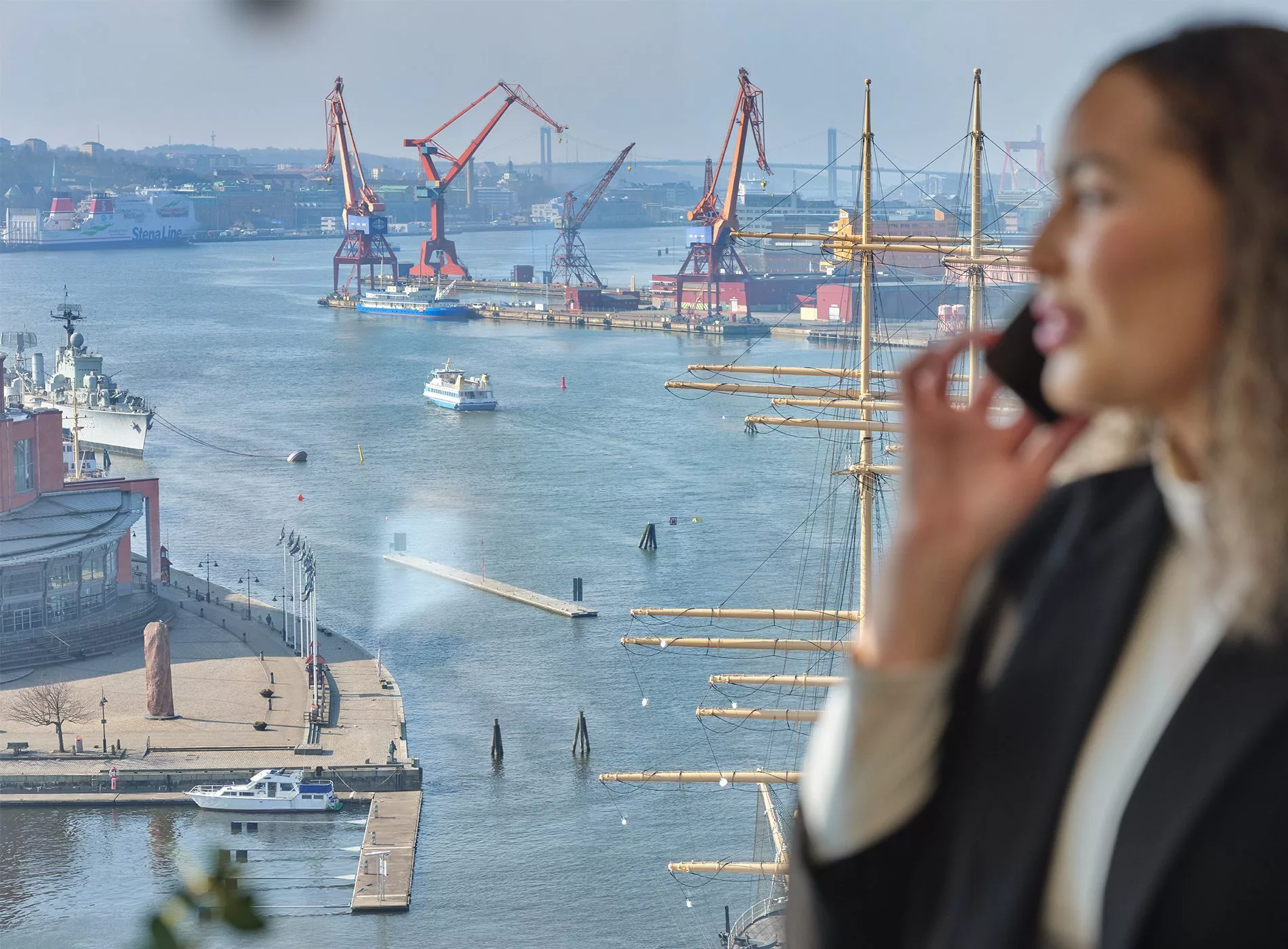 En suddigt foto av en kvinna som pratar i telefon med en hamn och kranar i bakgrunden.