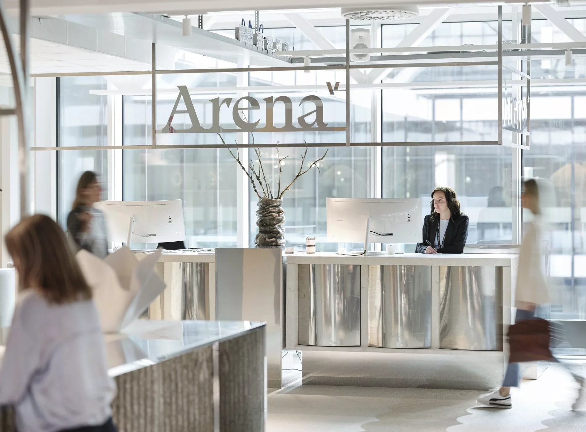 En receptionsdisk med texten "Arena" på glaset ovanför, och en receptionist som sitter bakom disken.