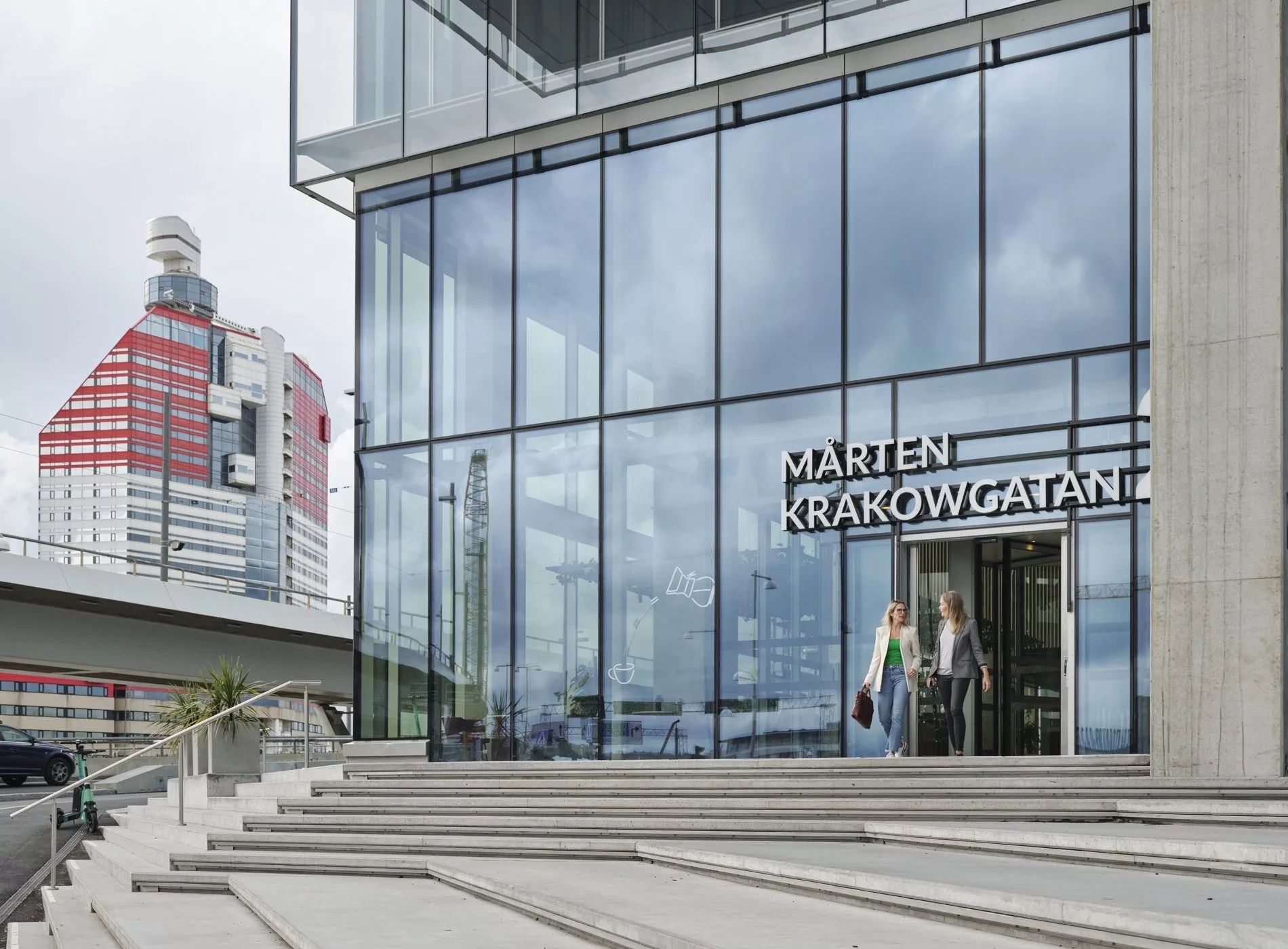 En modern byggnad med glasfasad och texten "Karten Kravongatan" vid entrén, trappor leder upp till dörren.