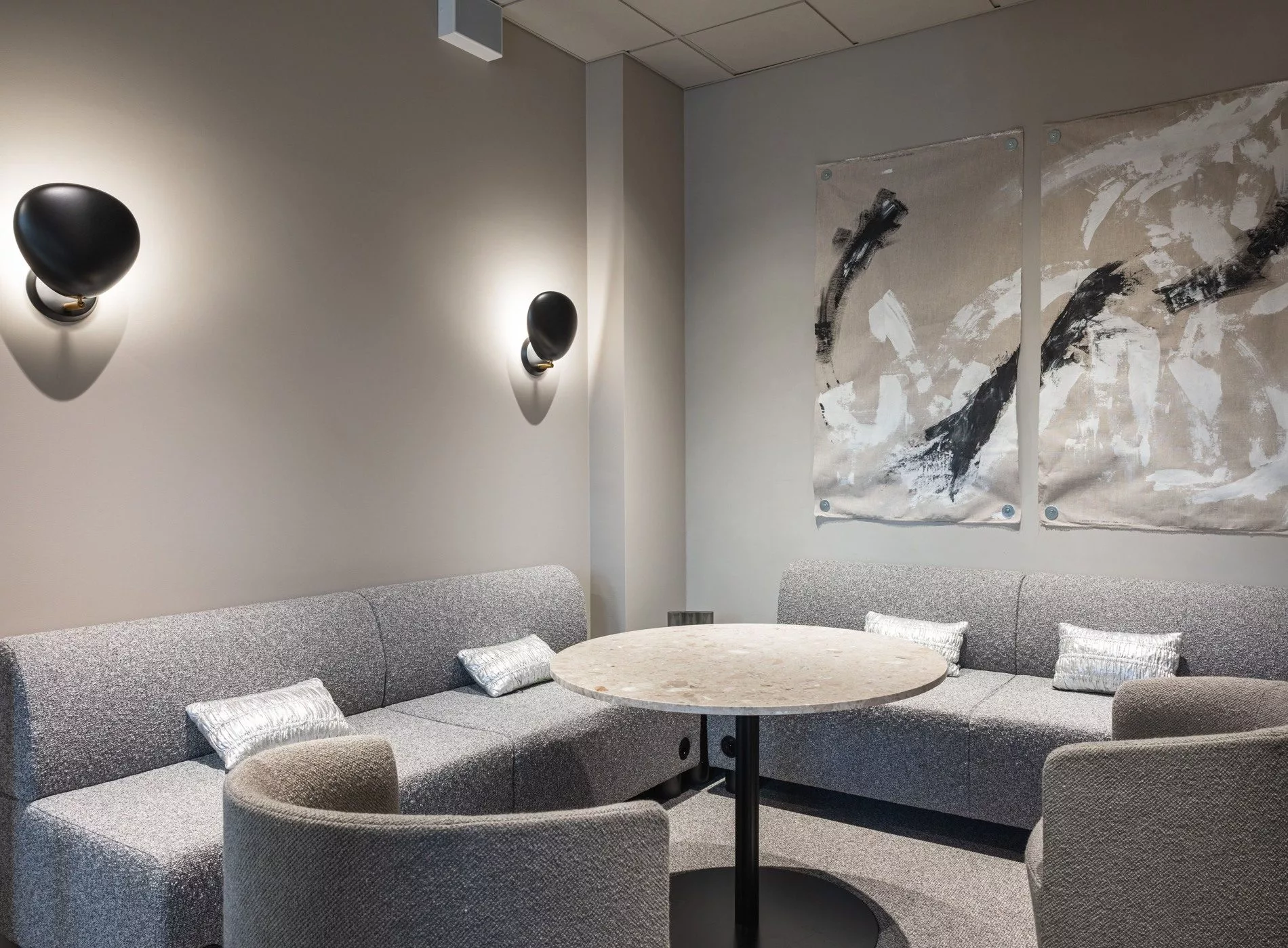 En sittgrupp med grå soffor, ett runt bord och abstrakt konst på väggen.