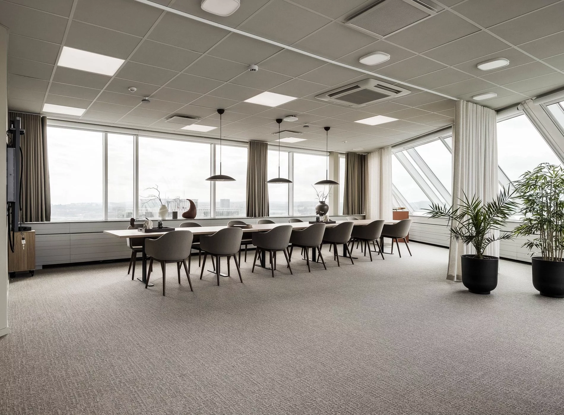 En modern möteslokal med lång konferensbord, beige stolar och stora fönster som släpper in dagsljus.