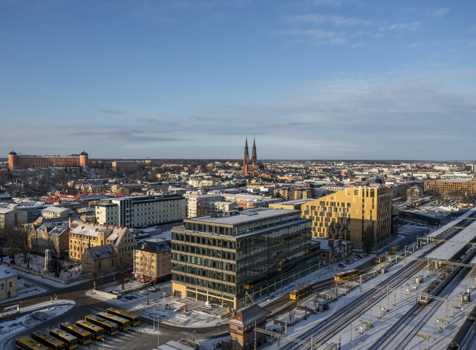 En stadsvy med moderna och äldre byggnader, snötäckta tak och kyrktorn i bakgrunden.