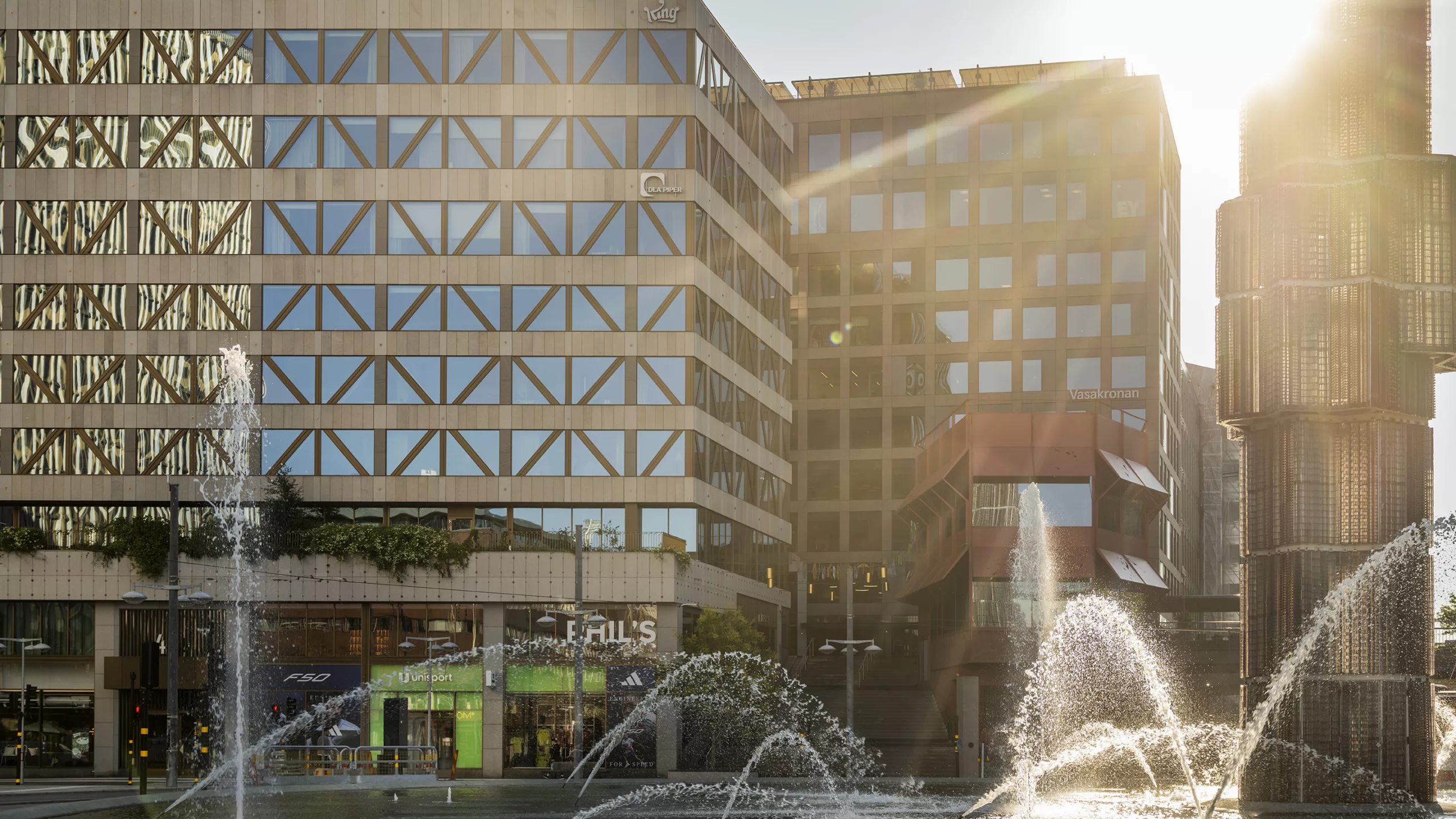 Byggnad med moderna glasfönster i solsken och en fontän i förgrunden.