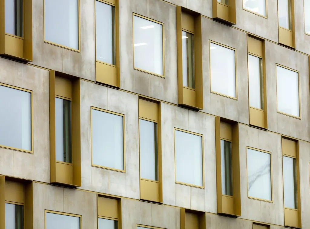 Fasad med flera rektangulära fönster i guld- och betongramar.