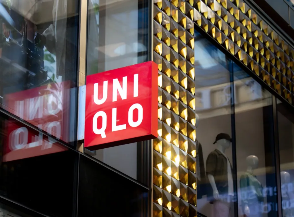 En skylt med texten "UNIQLO" på en fasad med gulddetaljer och glas.