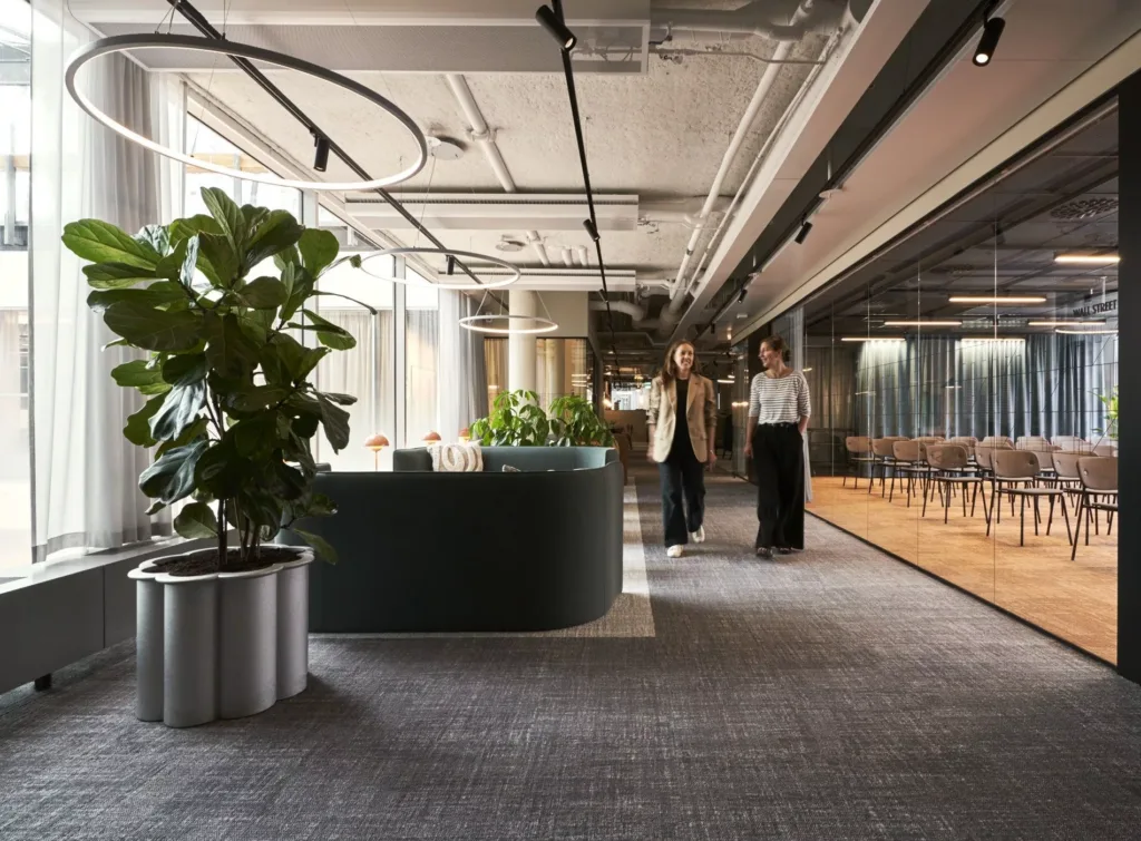 En reception med stora gröna växter och två personer som går genom ett modernt kontorsutrymme.