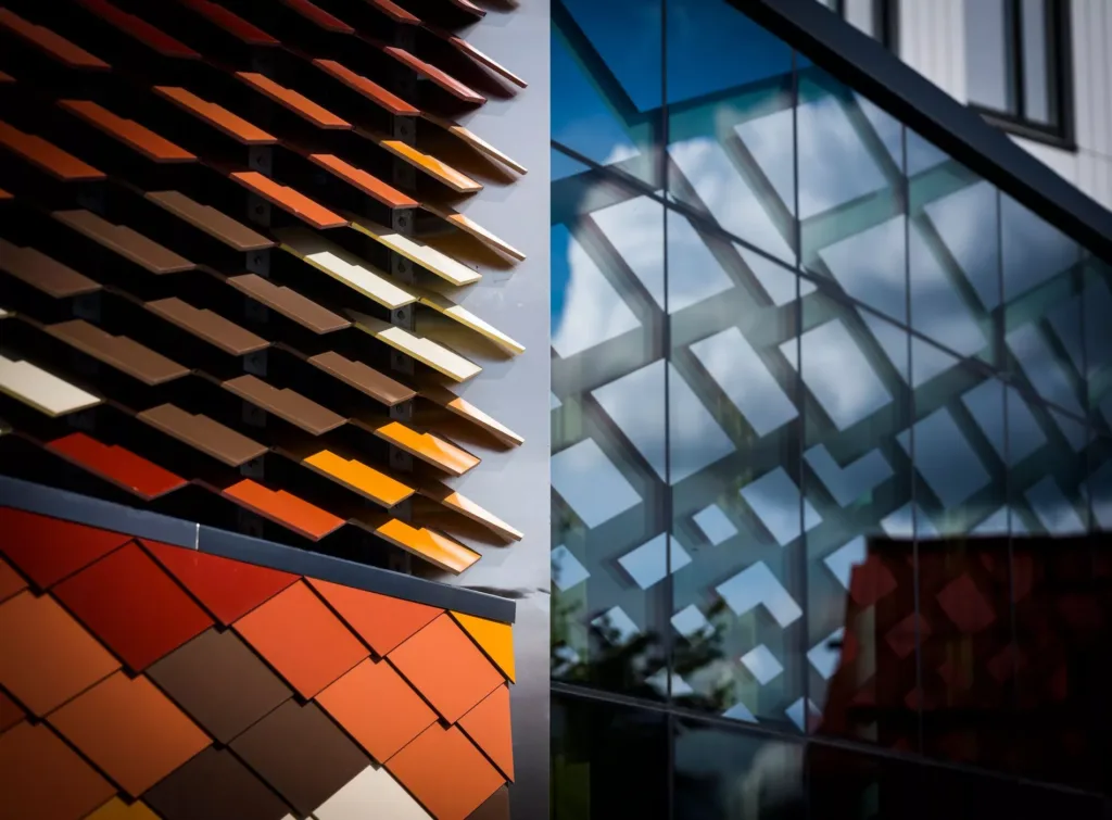Närbild på fasader med färgglada takplattor och glas med reflektioner av geometriska mönster.