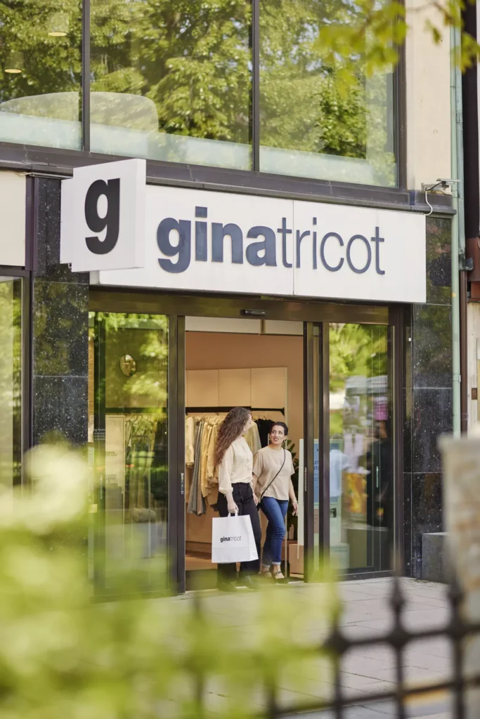 Två personer går ut från en Gina Tricot-butik, omgivna av grönska.