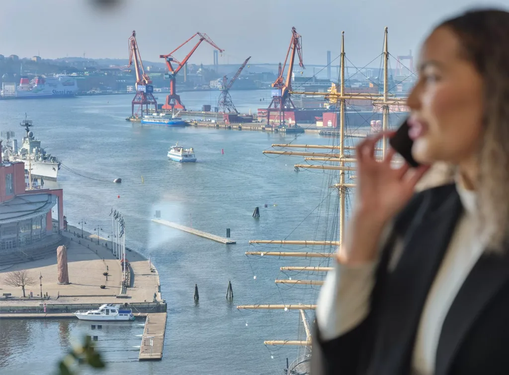 En suddig bild av en kvinna som pratar i telefon med en hamn och kranar i bakgrunden.