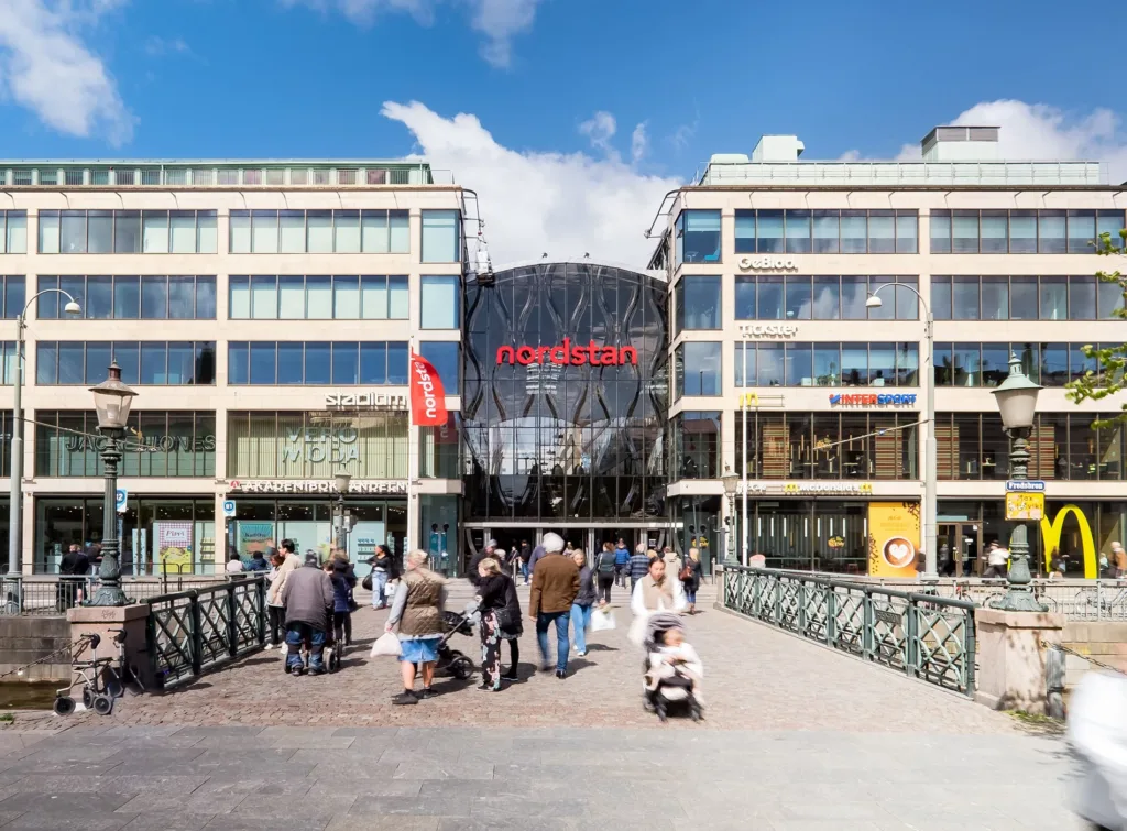 En grupp människor går över en bro mot en modern byggnad med skylttexten "Nordstan".