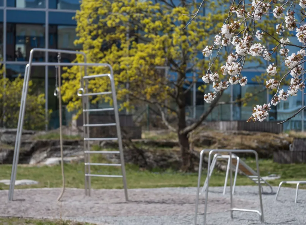5. En lekplats med metallställningar, gröna träd och ett blått glasbyggnad i bakgrunden.