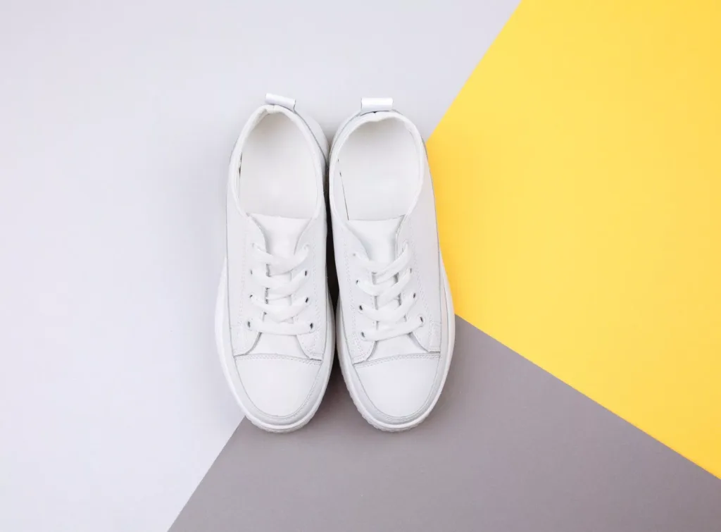 Ett par vita sneakers placerade på en bakgrund med gul, grå och vit färg.