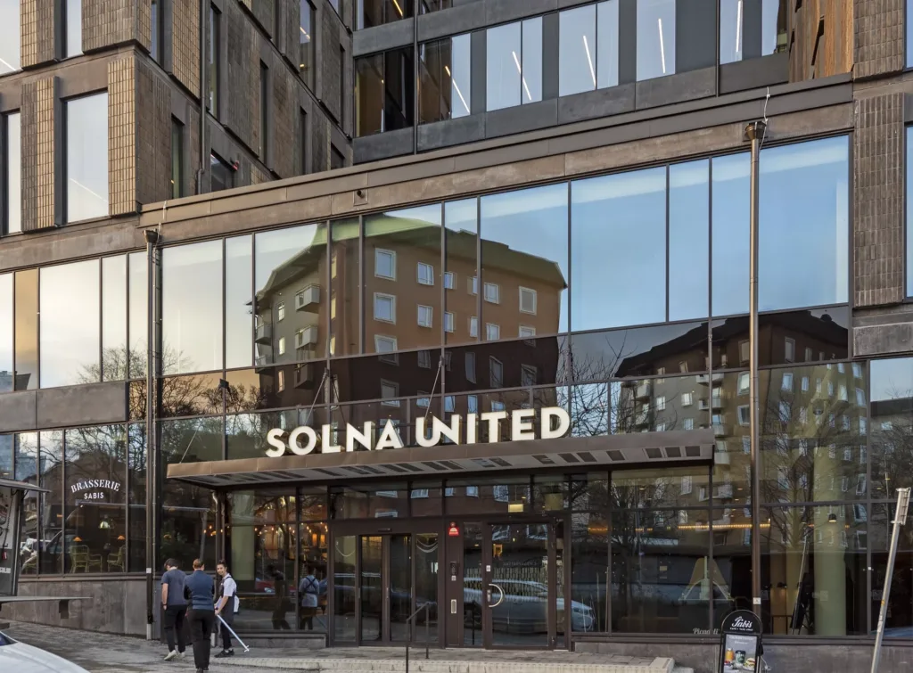1. Byggnad med glasfasad där texten "Solna United" är synlig; reflektioner av omgivningen visas på glaset.