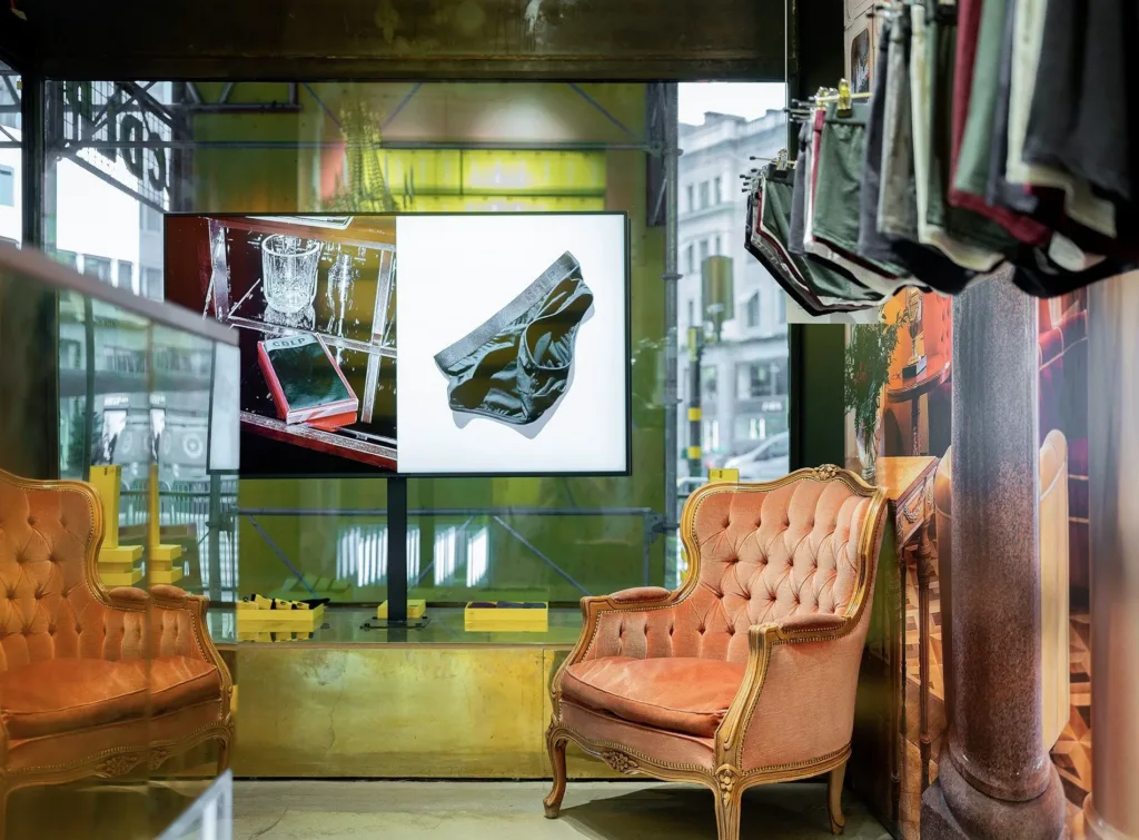 En elegant butik med en rosa fåtölj, tygprover och en bild på ett konstverk på väggen.