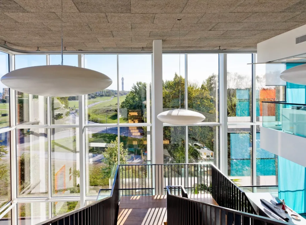 En modern byggnad med stora fönster, trappor och utsikt över grönska.