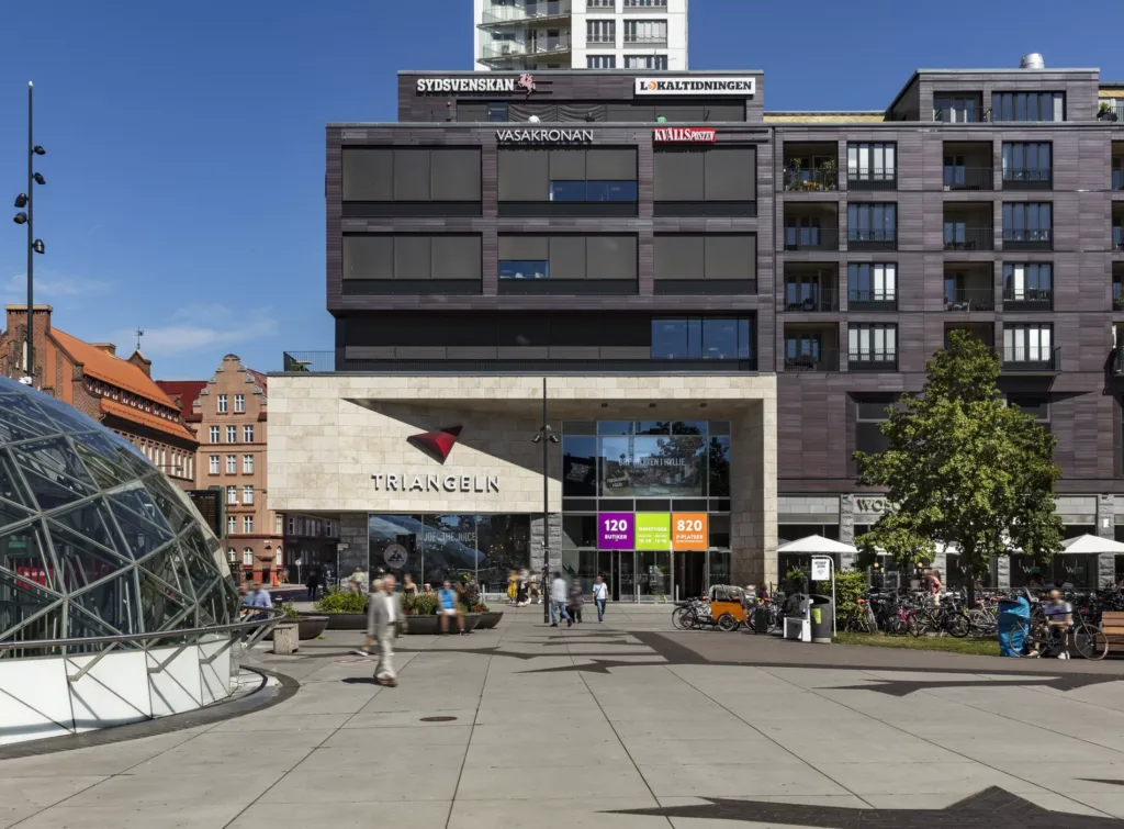 Ett modernt köpcentrum med glasfasad, färgglada skyltar och människor som promenerar utanför.