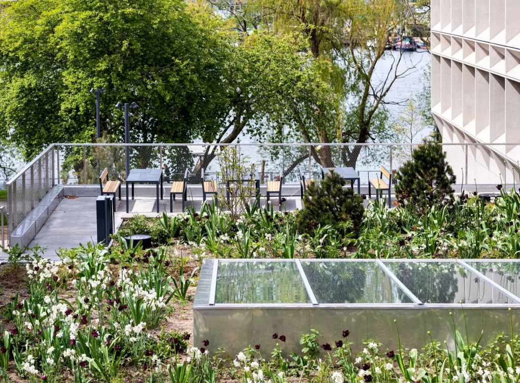 4. En trädgård med blommor och glasstrukturer, med utsikt över en sjö och träd.