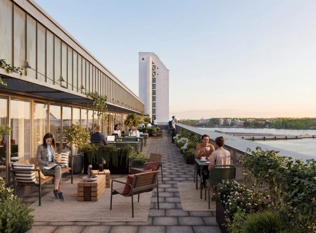 En takterrass med människor som sitter och umgås, omgivna av växter och möbler, med en utsikt över vatten och en annan byggnad.