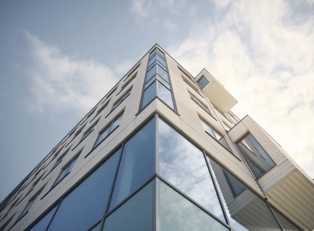 En modern byggnad med glasfasad fotograferad från marknivå mot himlen.