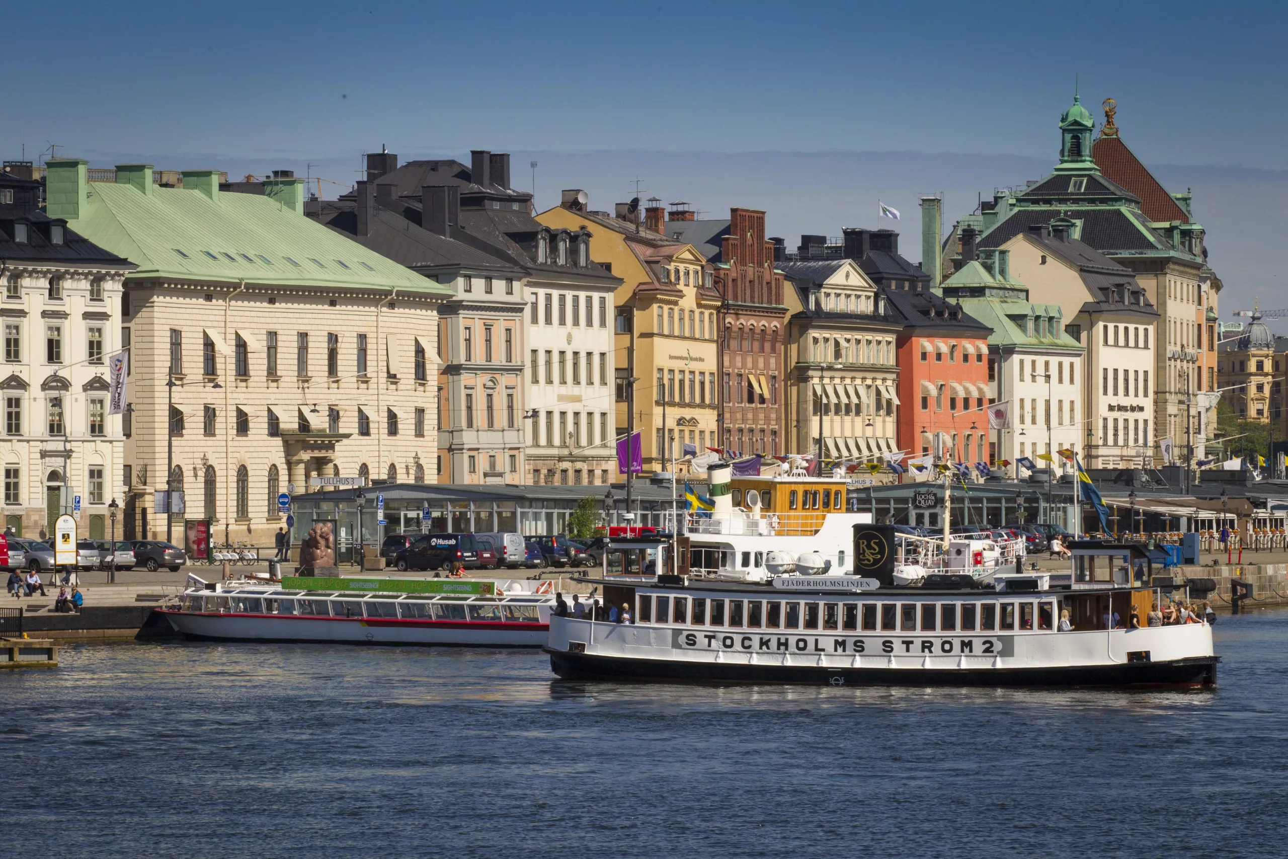 Flera färgglada byggnader vid en kaj, med båtar på vattnet.