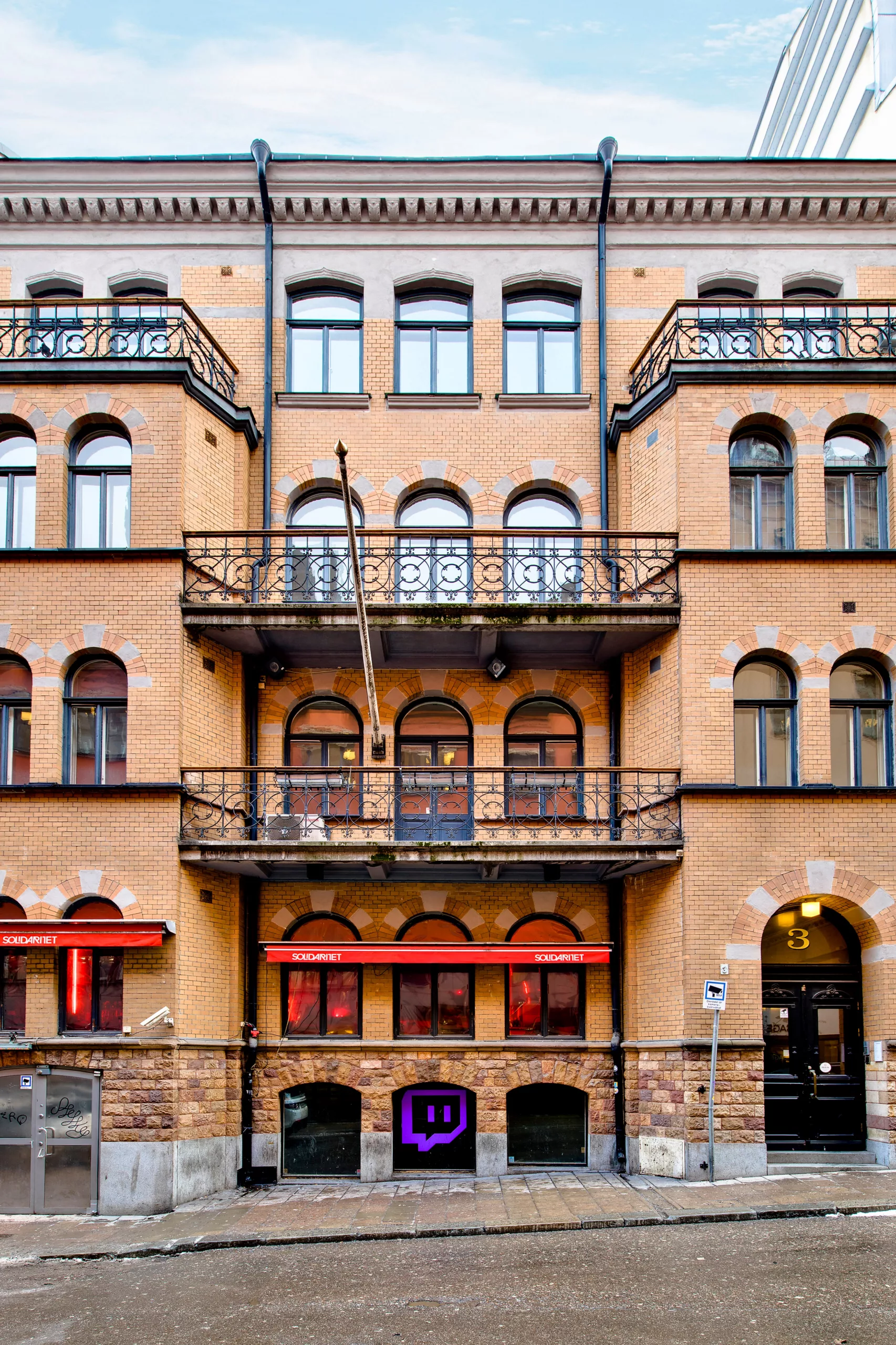 En äldre byggnad med symmetriska balkonger, välvda fönster och varma fasadfärger.