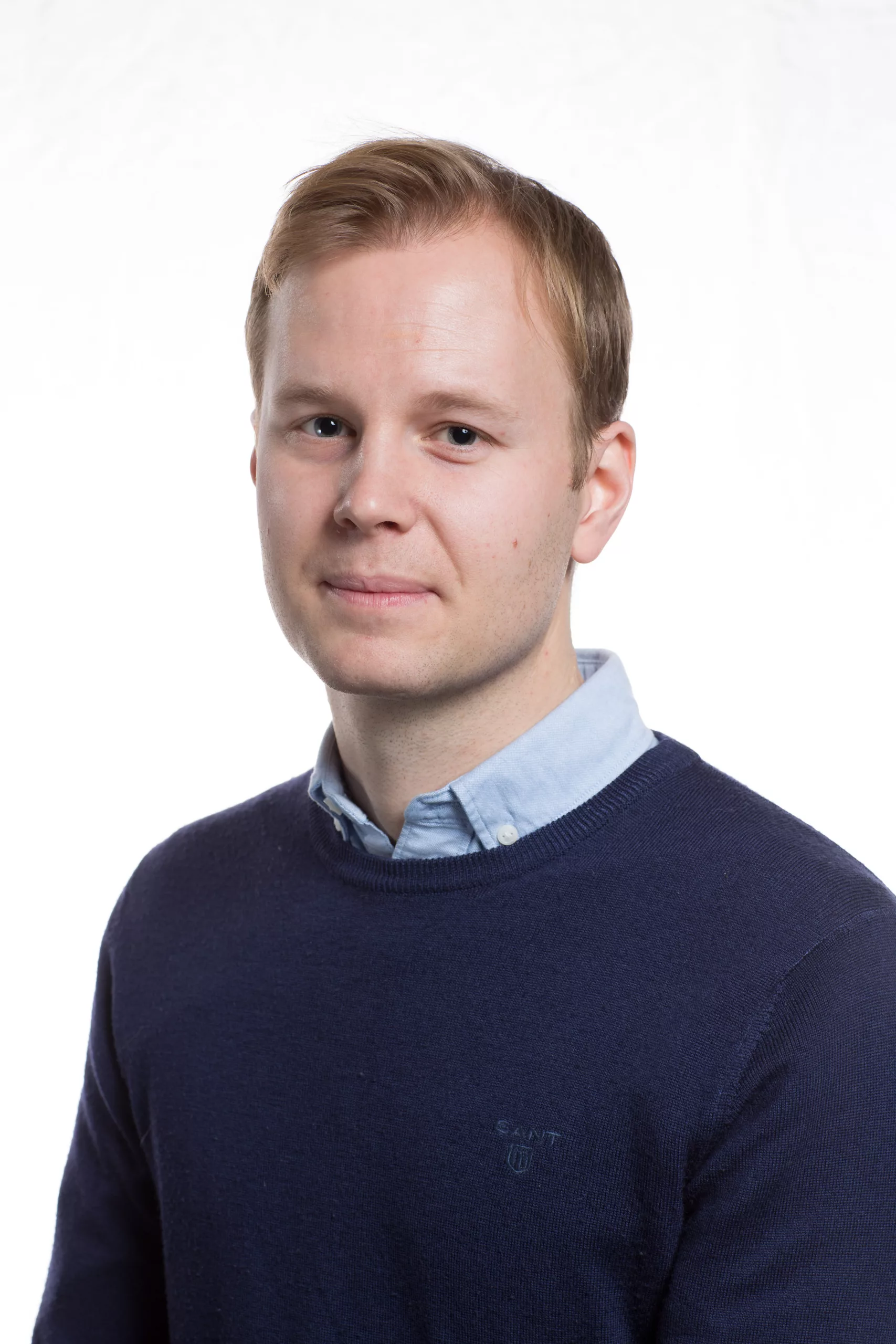 En person med kort hår, klädd i en blå tröja över en ljusblå skjorta, mot en vit bakgrund.