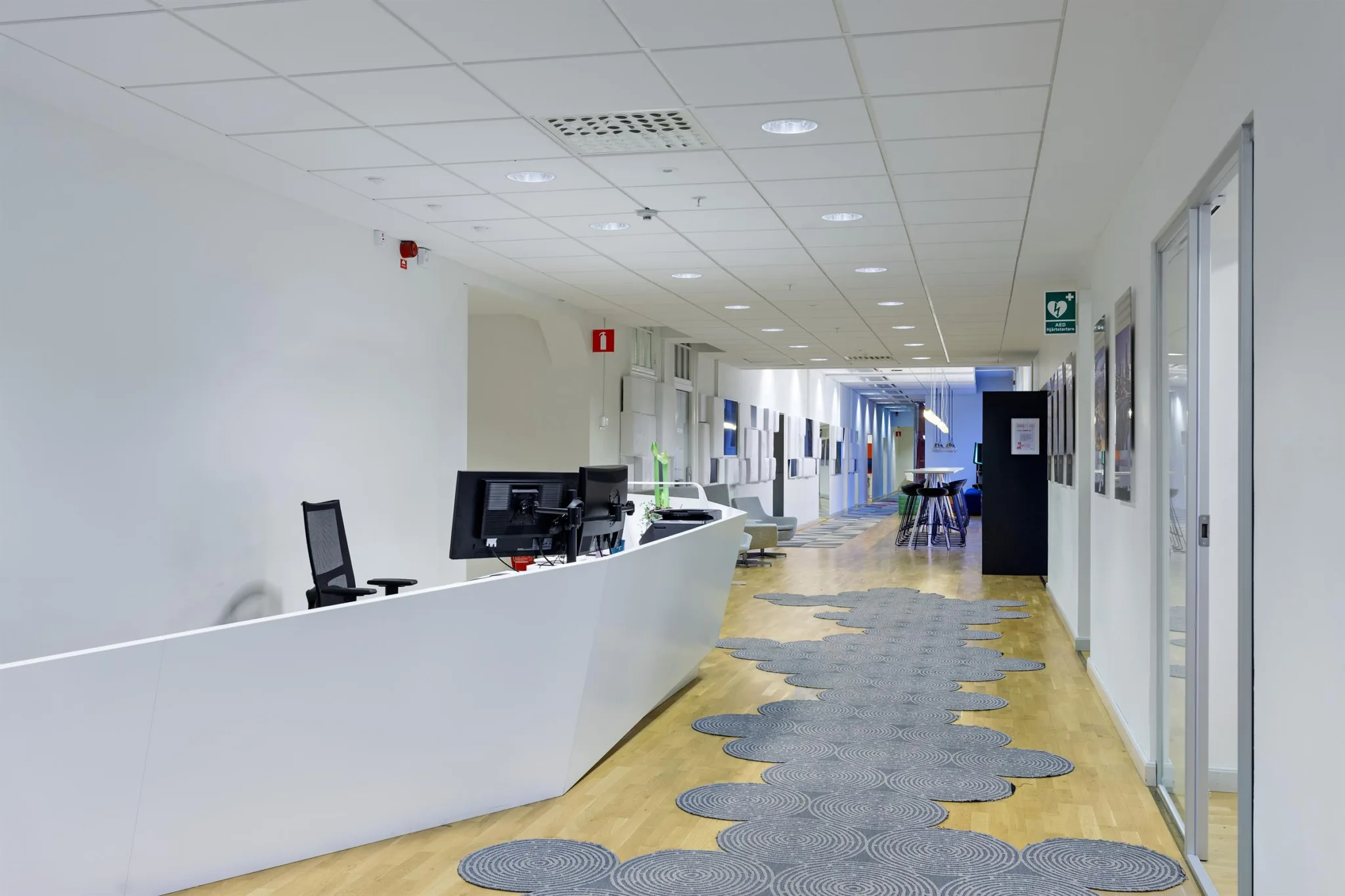 1. En reception med vit disk, datorskärmar och en korridor med ljus belysning och mönstrad matta.