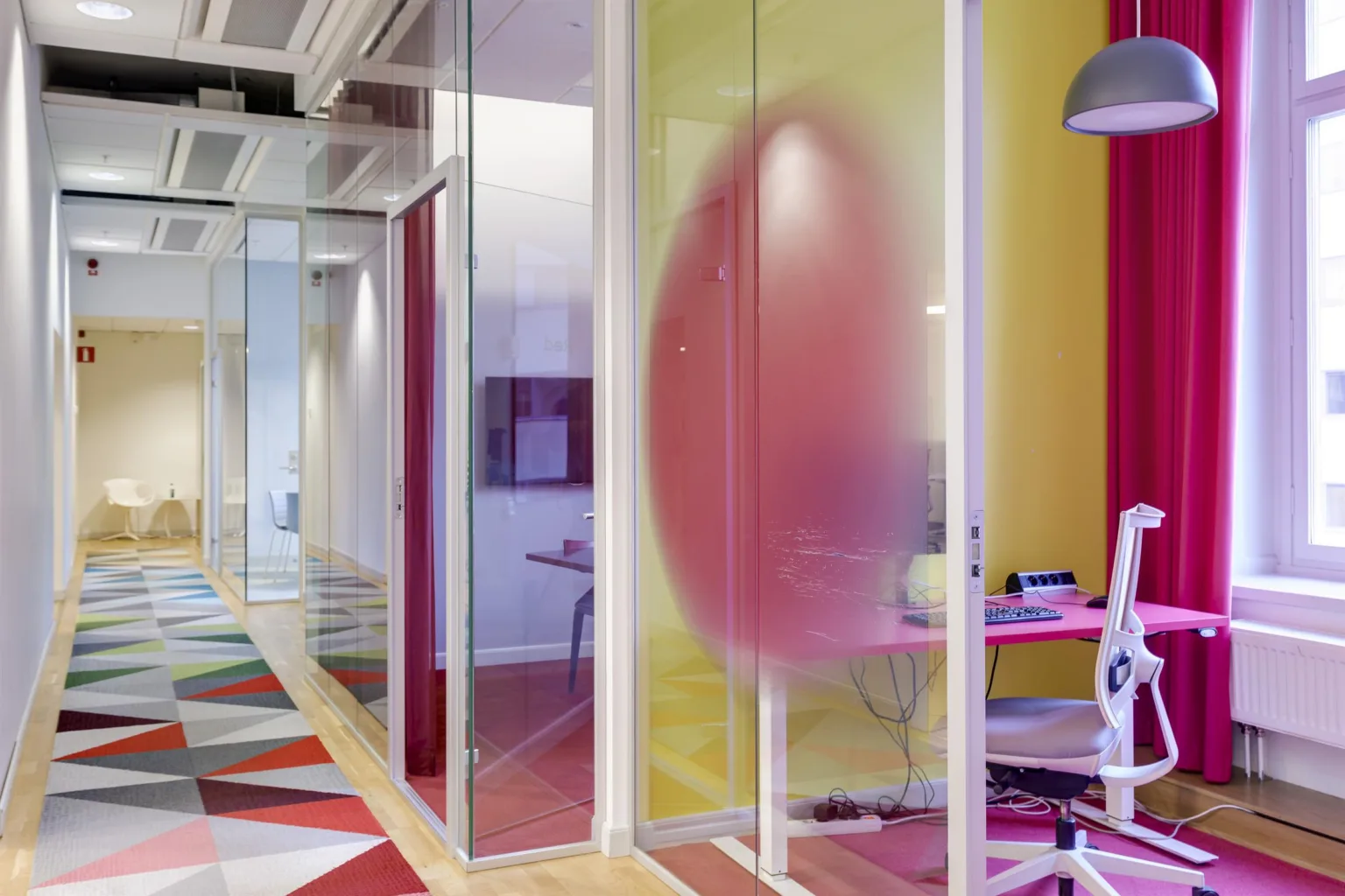 2. Ett kontorsområde med glasväggar, färgglada väggar och möbler, samt en rosa tonad design på glaset.