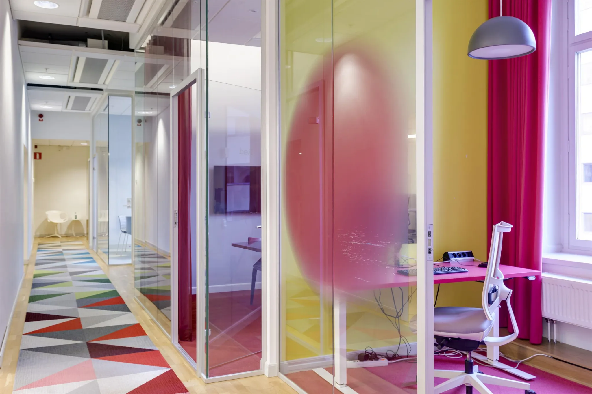 2. Ett kontorsområde med glasväggar, färgglada väggar och möbler, samt en rosa tonad design på glaset.