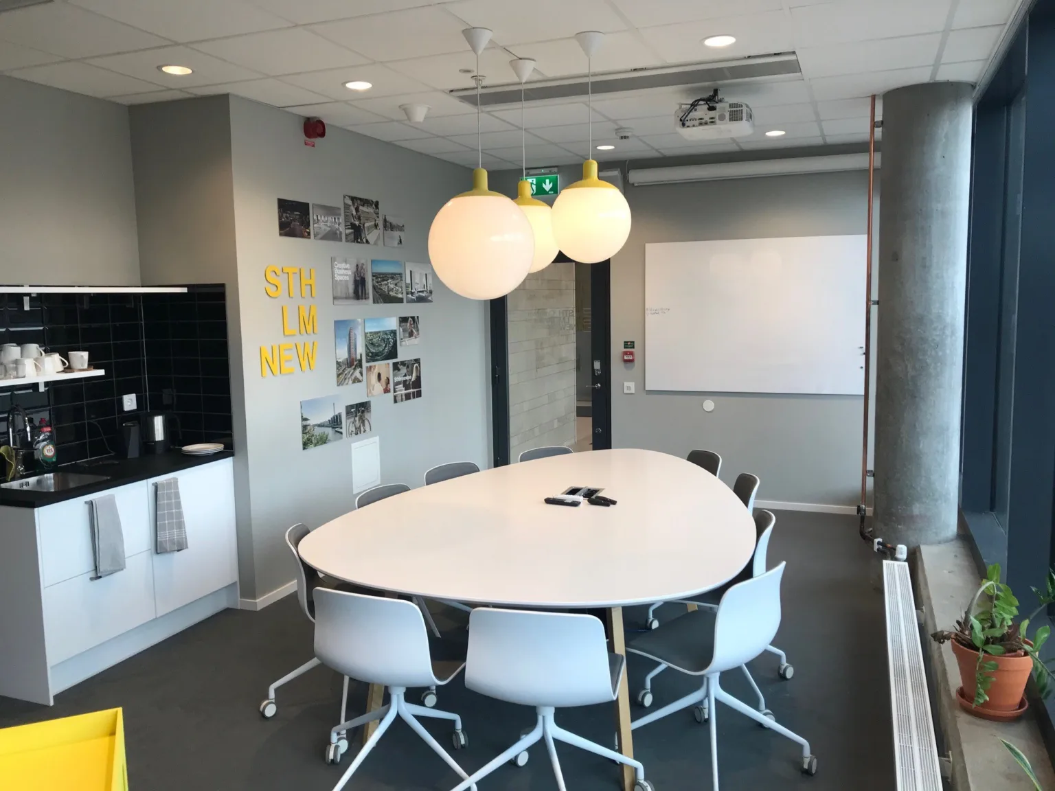 5. Ett mötesrum med ett ovalt bord, vita stolar, en whiteboard och dekorativa lampor.