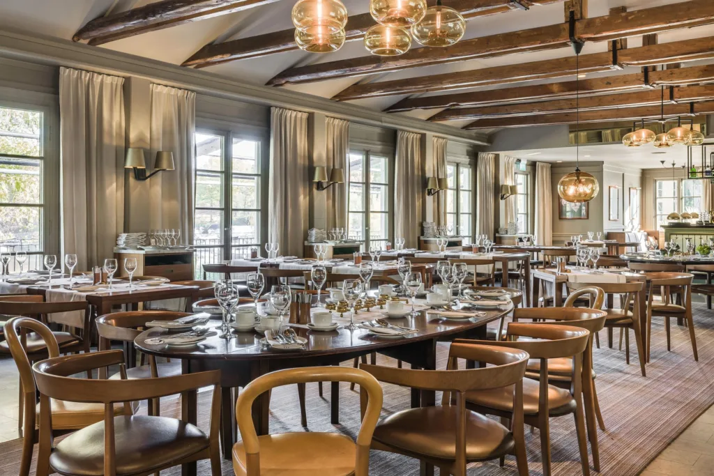 2. En elegant restaurang med dukade bord, trästolar och hängande lampor i ett rum med stora fönster.