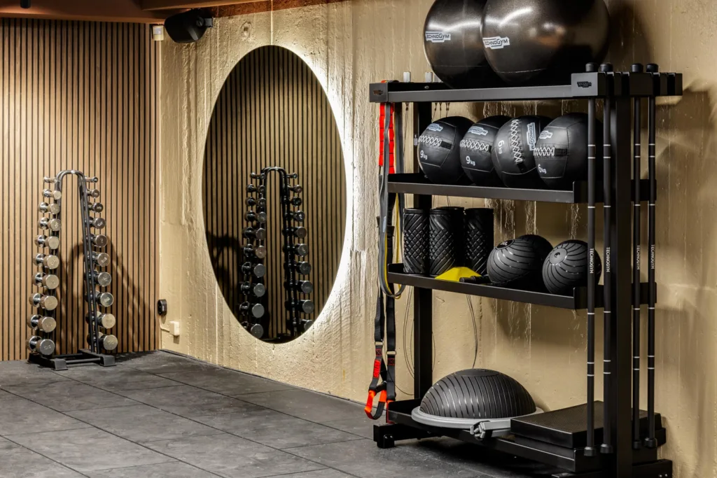 5. Ett gym med en spegel, hyllor med medicinbollar och träningsutrustning på väggen.