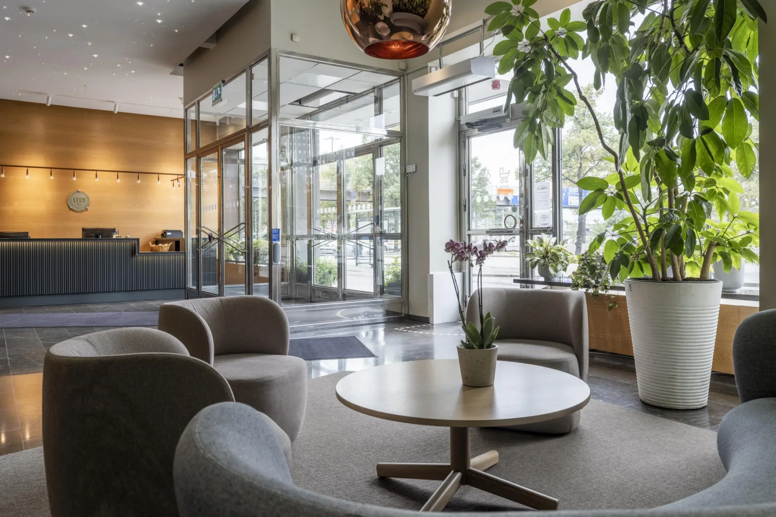 - En ljus hotellobby med sittgrupper, växter och glasdörrar.