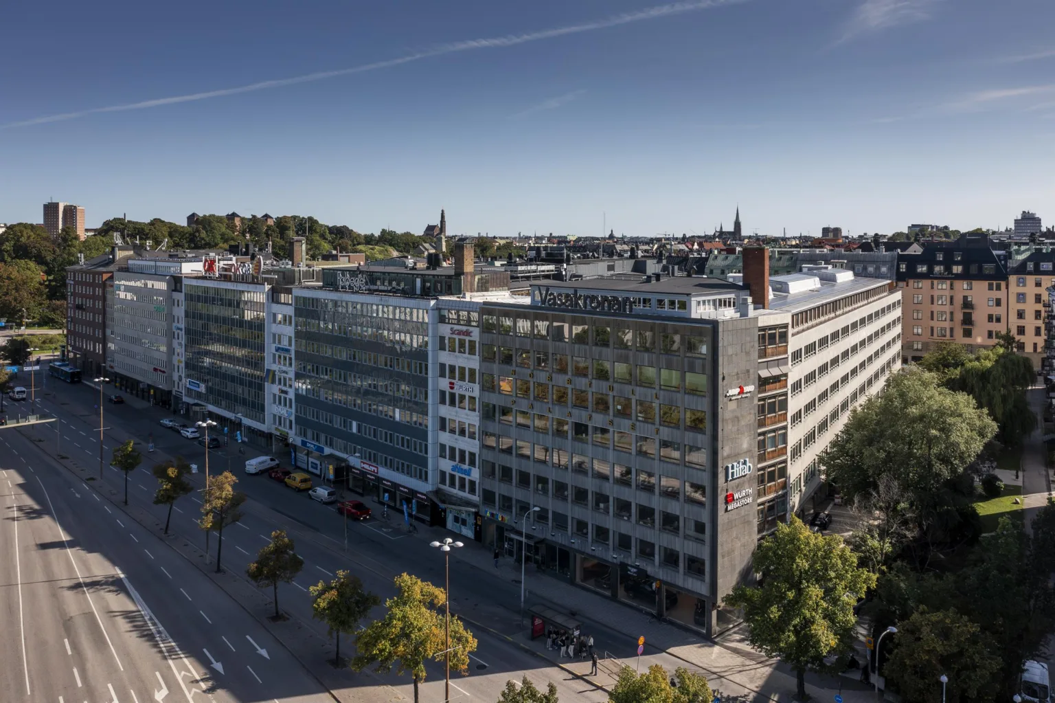 - En stor kontorsbyggnad med glasfasad, omgiven av träd och en blå himmel.