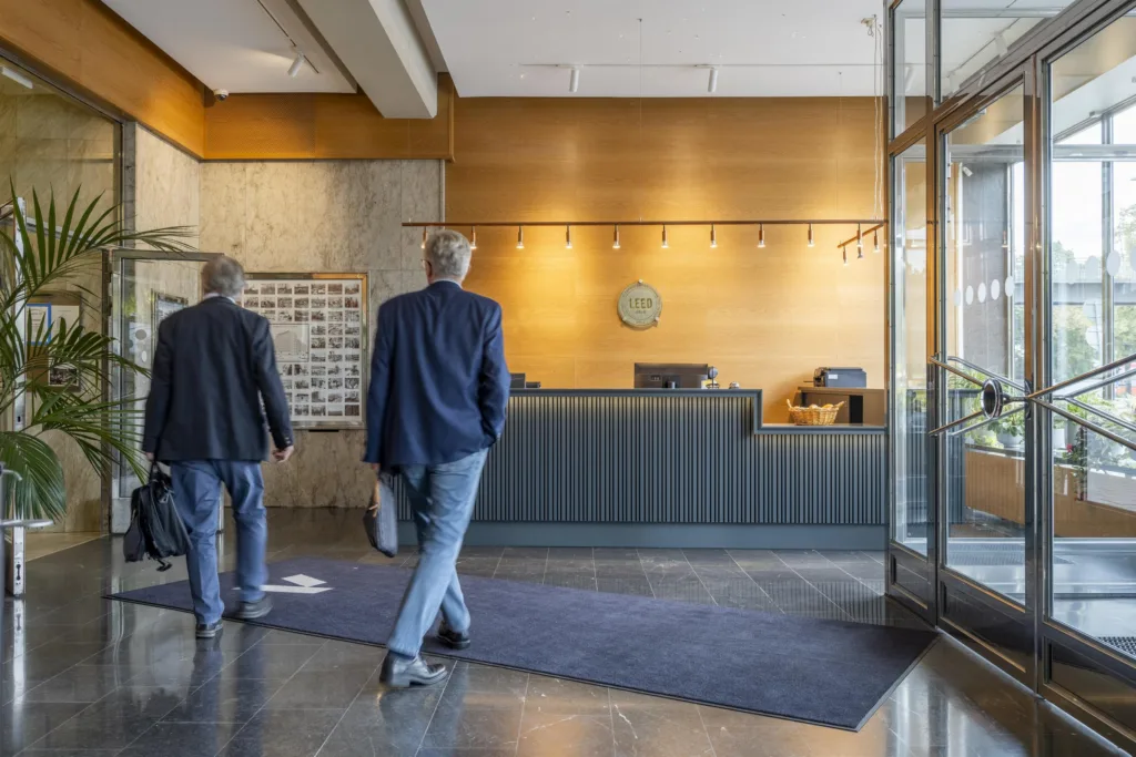 1. Två personer går mot en receptionsdisk i ett hotell med en modern och ljus inredning.