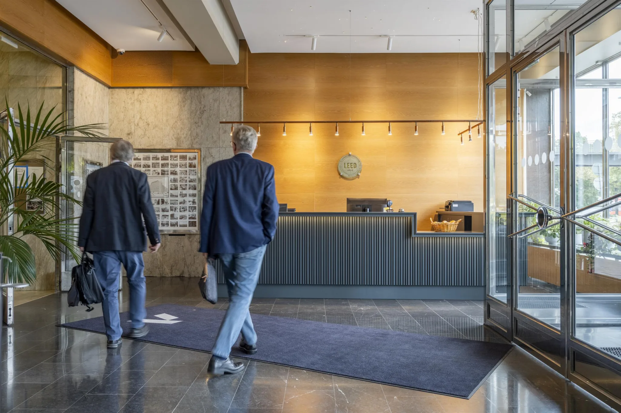 4. Två män i kostymer som går mot en receptionsdisk i en ljus och modern byggnad.