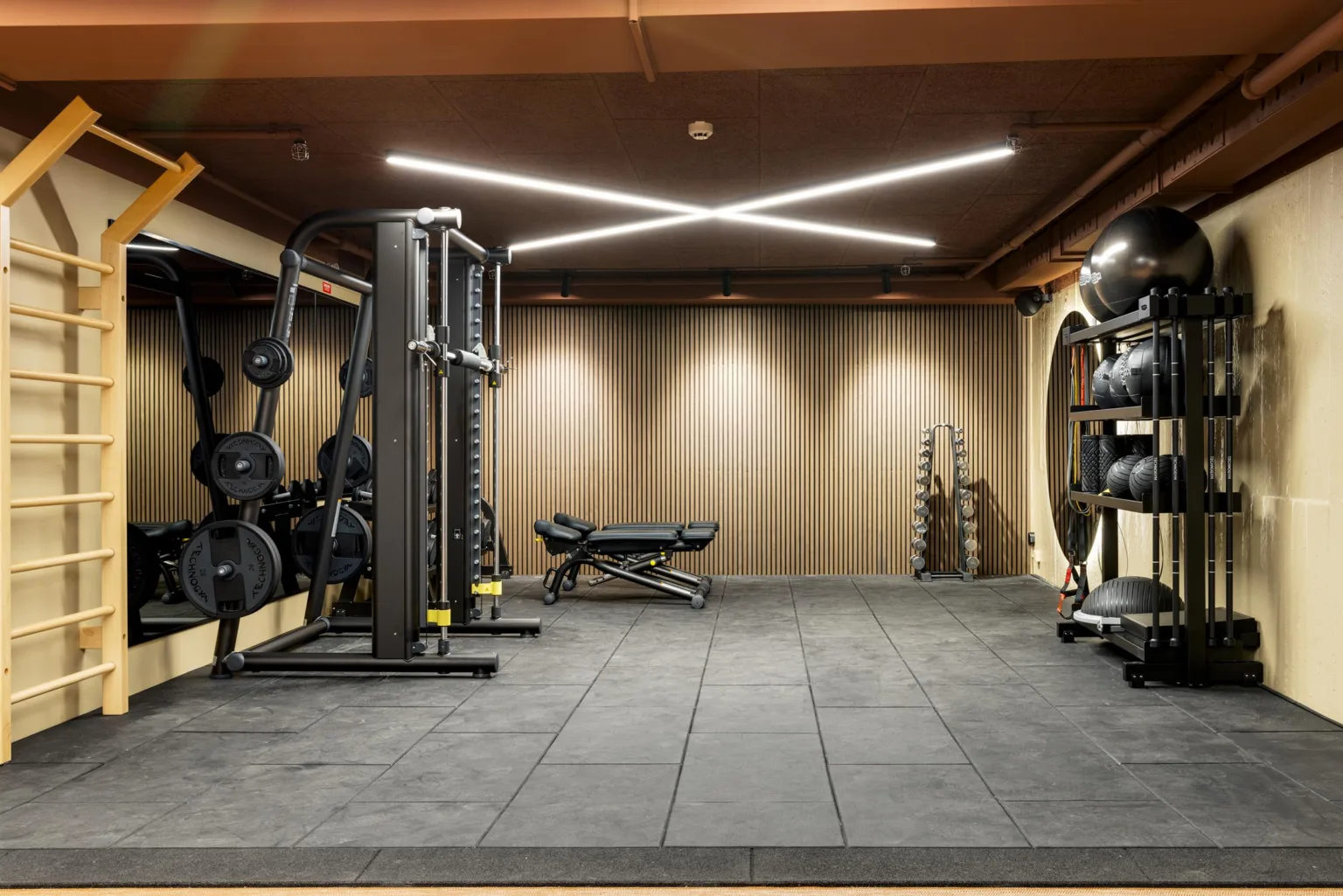 Ett gym med fria vikter, träningsmaskiner och en bänk, belyst av moderna taklampor.