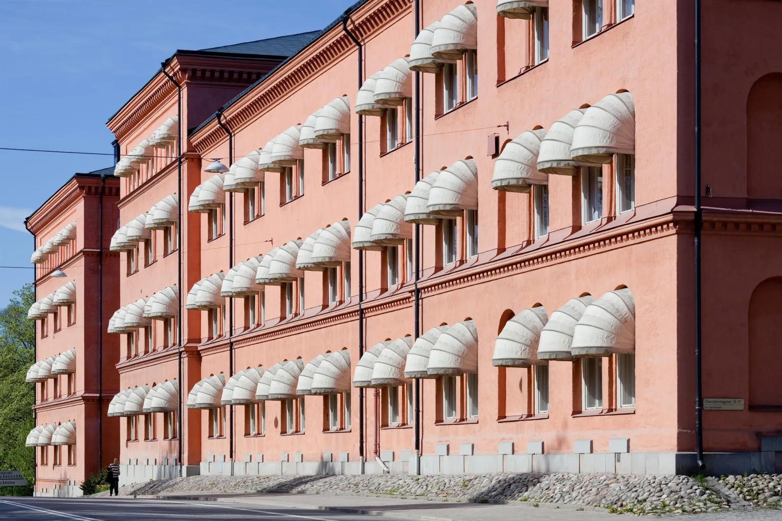 En lång rosa byggnad med många välvda fönster och vita fönsterskydd.