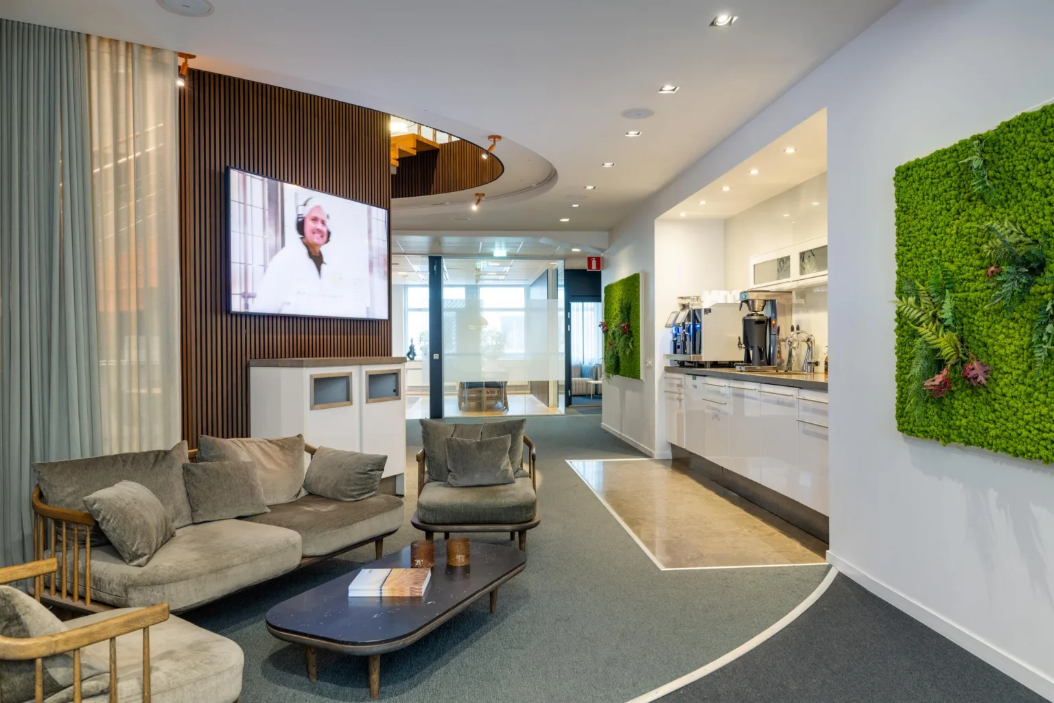 Ett loungeområde med soffor, ett lågt bord, en väggmonterad TV och ett pentry i bakgrunden.