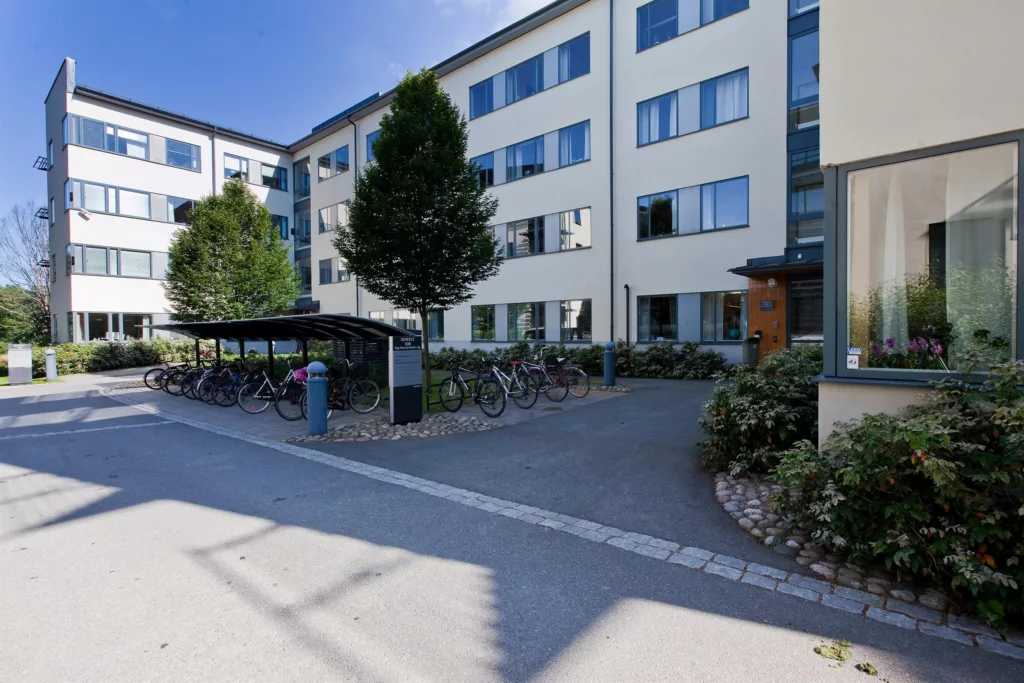 - En modern byggnad med flera våningar, omgiven av cykelställ och grönska.