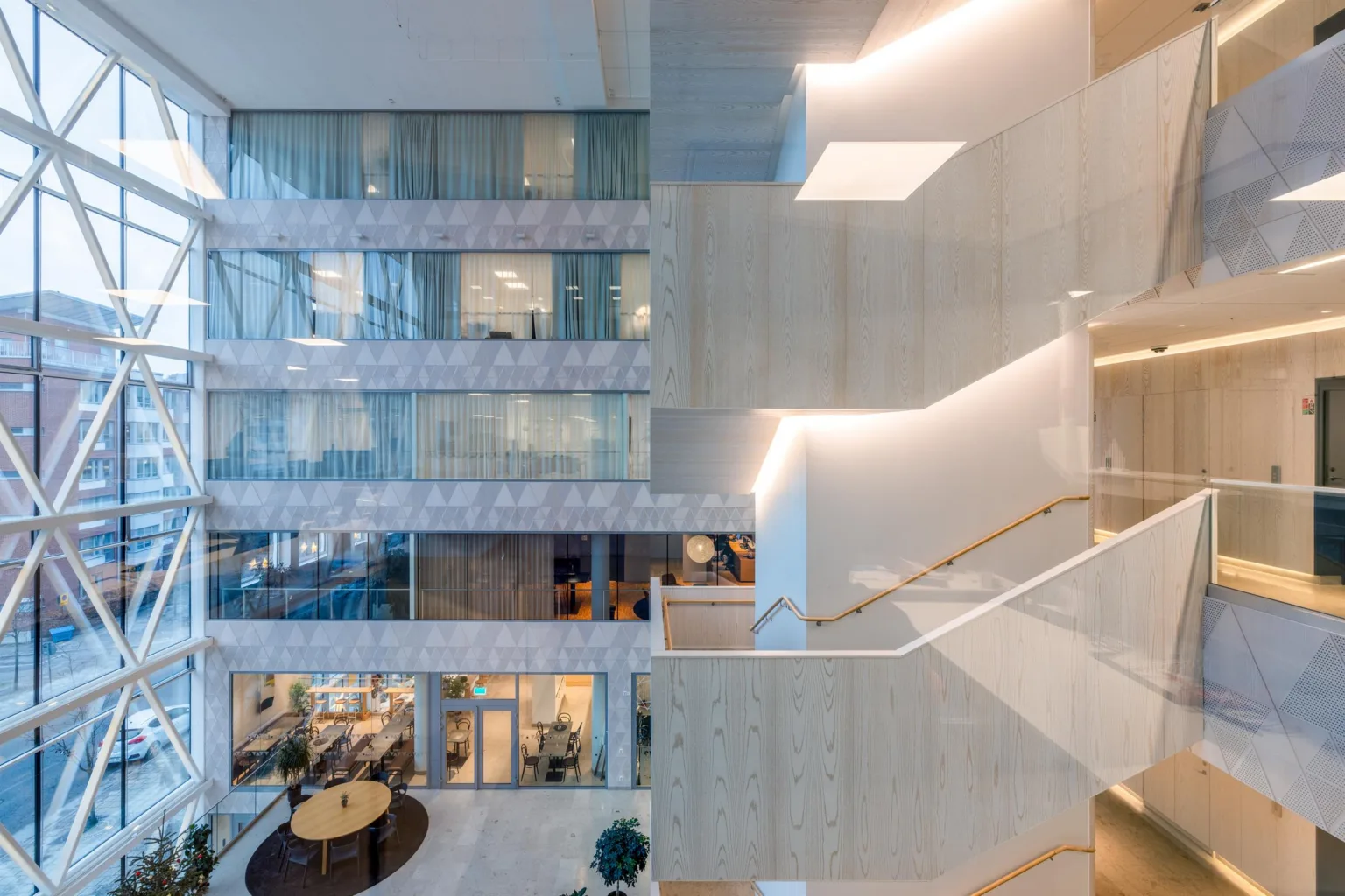 En öppen byggnadsdesign med flera våningar, glasväggar och en trappa med stilren belysning.