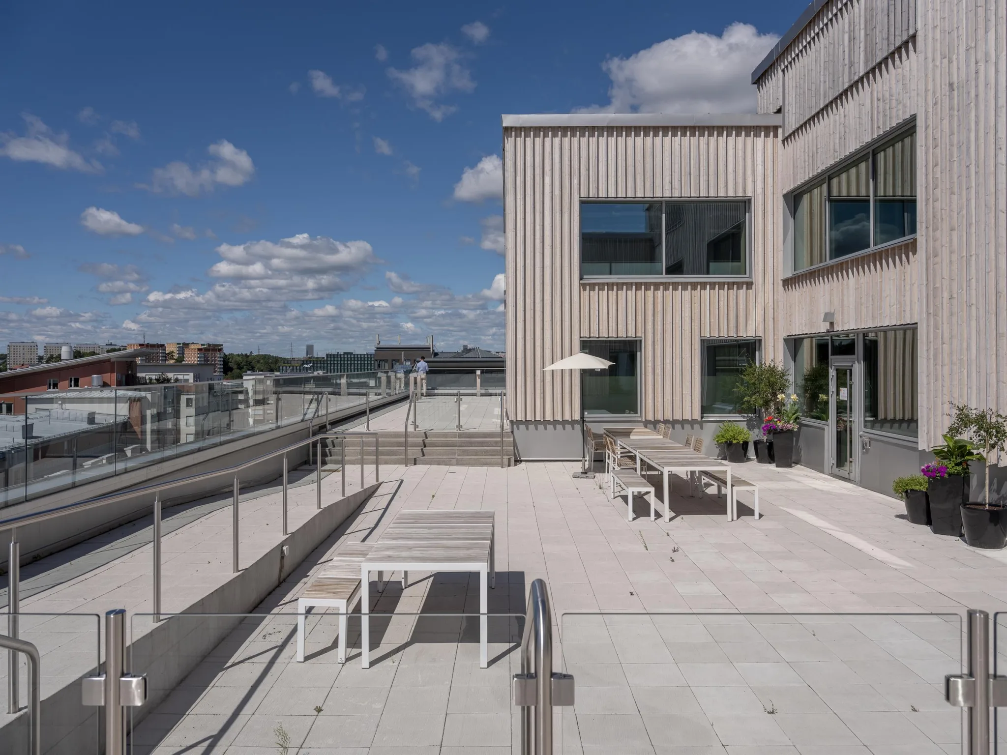 2. Stor takterrass med möbler, parasoll och utsikt över staden under en klarblå himmel.