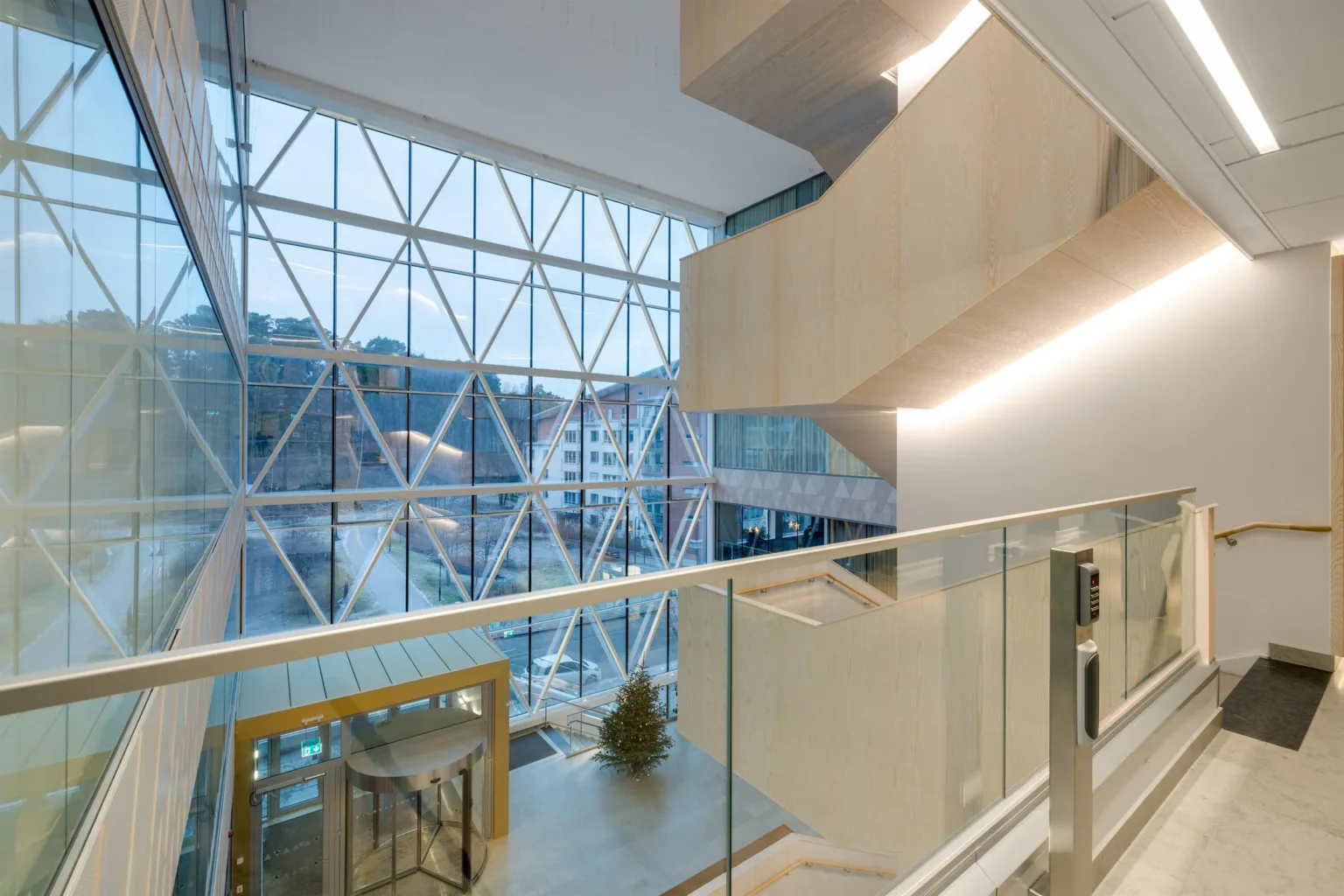 En modern byggnad med glasfasad, utsikt över stadsmiljö och trappa med ljus belysning.