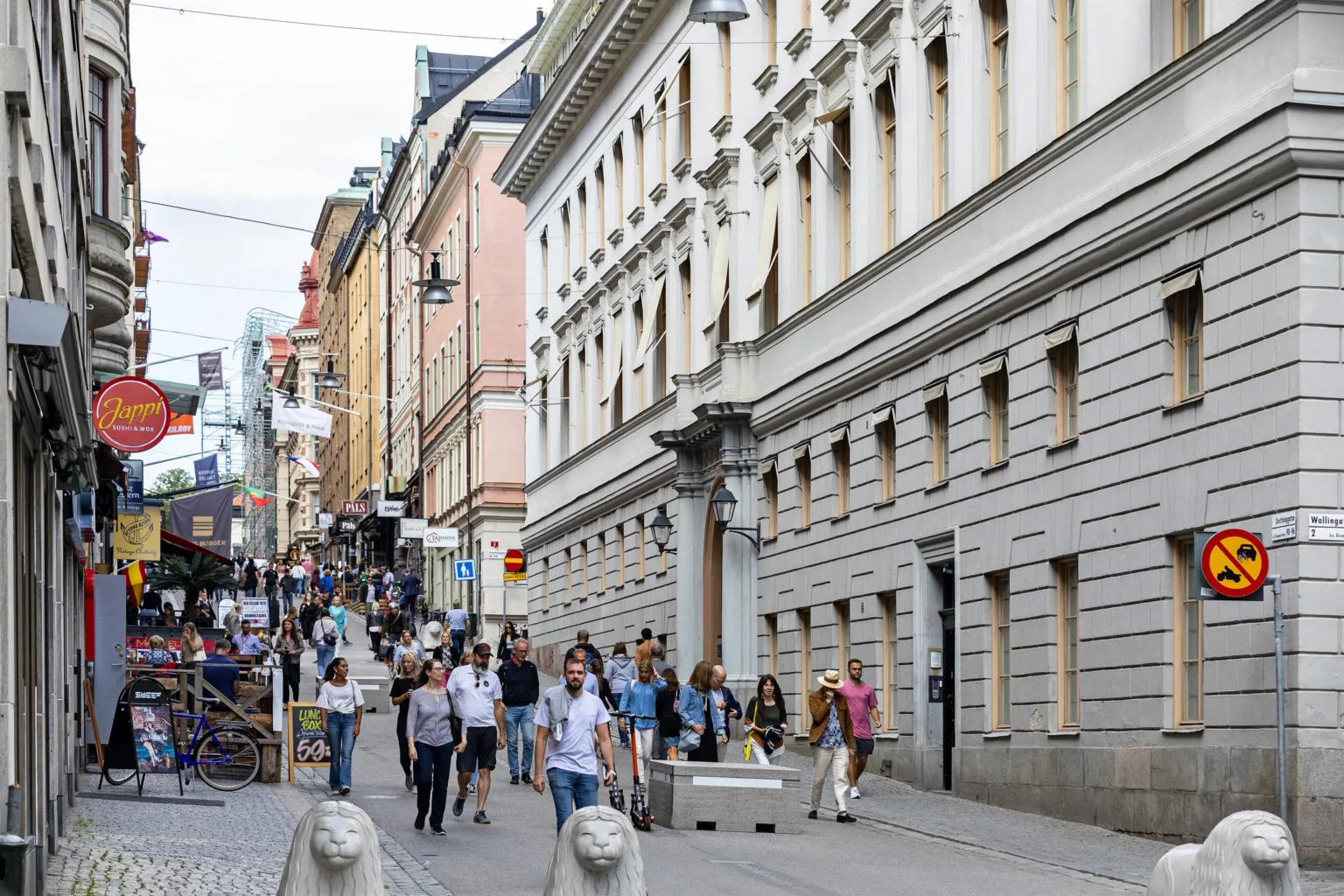 En gata fylld med människor som går, omgivna av äldre byggnader med detaljerade fasader.
