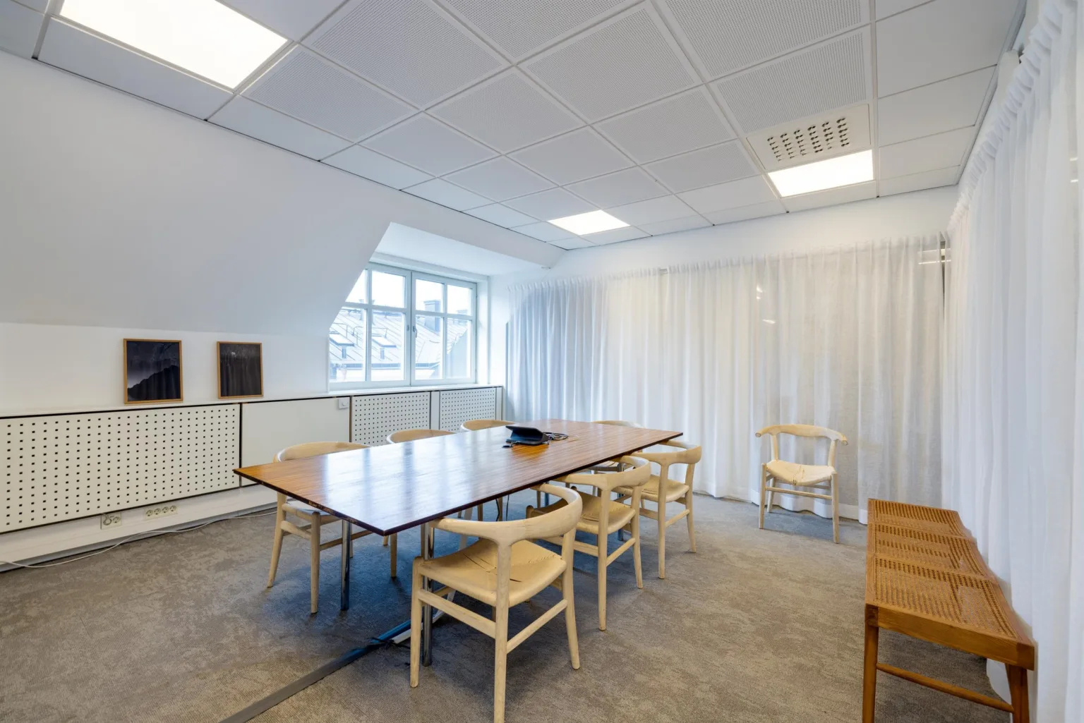 Ett mötesrum med ett stort träbord, trästolar och gardiner som täcker en vägg.