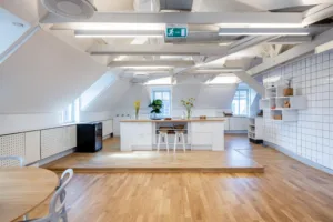 4. Ett modernt kök med stora bänkar, vita skåp, blommor och barstolar på en upphöjd plattform.