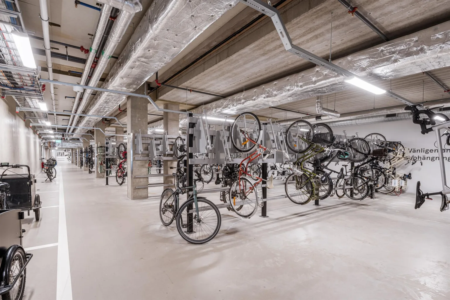 Ett cykelgarage med flera cyklar parkerade i rad under ett betongtak.